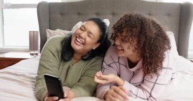 Anne ve kız, haber verildiğinde yatak başlığıyla yatıp, akıllı telefonları kaydırıyor ve gülüyorlar. Aile, kaynaşma, boş zaman, sıcak, samimi, modern, bağ