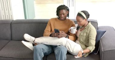 Eve girerken, Afrikalı Amerikalı çift telefonları kaydırıyor, uzaktan kumandayı kontrol ediyor ve içeriği paylaşıyorlar. Samimi, samimi, teknoloji, rahatlama, iletişim, çağdaş, yaşam tarzı