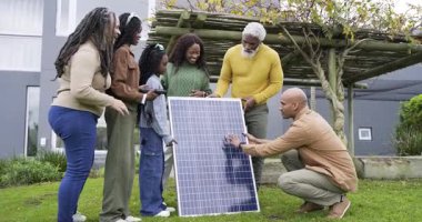 Çeşitli aileler ve teknisyenler arka bahçedeki tablet tıkırdatma ve öğrenme paneline güneş paneli yerleştiriyor. Yenilenebilir, enerji, teknoloji, sürdürülebilirlik, çevre dostu, eğitim, açık hava