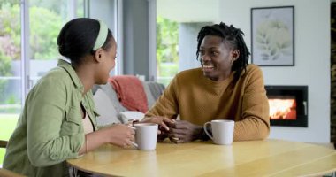 Afrika kökenli Amerikalı bir çift, beyaz bardaklarla kadın üstüne kadın yakalayıp oturma odasında el kol hareketi yapıyor. Samimiyet, sohbet, ev, rahatlama, sıcaklık, bağlantı, modern