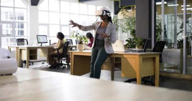 Hintli bir kadın ofiste masasında sanal gerçeklik kulaklığı takarak 3 boyutlu menüleri ve kopyalama alanını araştırıyor. Futuristik, işbirliği, teknoloji, yenilik, çalışma alanı, dalgın, profesyonel