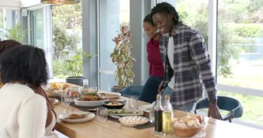 Sohbet duymak, farklı arkadaşların yemek masasının etrafında toplanması, sandalye çekmesi, yeşil fasulye geçmesi. Misafirperverlik, dostluk, kutlama, sosyalleşme, ev hanımı, hayat dolu, toplum.