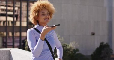 Afrika kökenli Amerikalı bir kadın akıllı telefonu çalıştırıyor korkuluklara yaslanıyor çatıdan sesli mesaj gönderiyor. Kentsel, iletişim, yaşam tarzı, modern, gündelik, canlı, açık hava