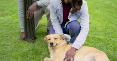 Arka bahçede altın köpek gören farklı arkadaşlar, gülümseme alışverişi yaparken diz çöküp oynaşıyorlar. Evcil hayvanlar, arkadaşlık, açık hava, eğlence, sevgi, uyum, arkadaşlık.