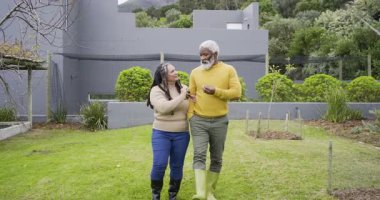 Kıdemli çift bahçeye çitten giriyor ve fidan bakımını planlamak için kamera önünde dolaşıyorlar. Aile, arkadaşlık, sürdürülebilirlik, bahçıvanlık, açık hava, yaşam tarzı, doğa