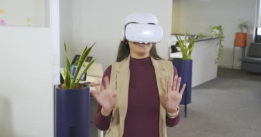 VR kulaklık takan, orta yaşlı bir kadın ofis salonunu keşfetmek için el işaretleriyle sanal alemde geziniyor. Teknoloji, yenilik, sürükleyici, fütürizm, işbirliği, profesyonel, gösterişli