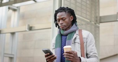 Afro-Amerikalı bir adam plazada kahve ile telefon uyarısı alıyor, ekranı dinliyor ve çağrıya cevap veriyor. Kentsel, modern, teknoloji, yaşam tarzı, profesyonel, çağdaş, açık hava