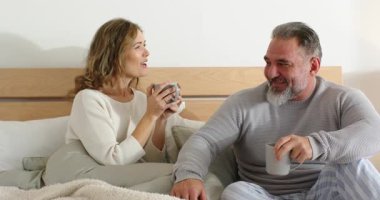 Çift sabah kahvesini yatak odasında paylaşıyor. Sonra kadın gülümsüyor, kupayı yudumluyor, keyif alıyor. Samimiyet, kahvaltı, rahatlama, arkadaşlık, konfor, bağlantı, sade