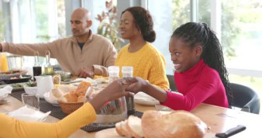 Çeşitli aileler el ele tutuşup birlikte dua ediyor sonra da kahvaltıya başlamak üzere yemek masasına meyve suyu döküyorlar. Aile bağı, sabah rutini, aile sahnesi, sağlıklı, rahat, doğal ışık, birliktelik.
