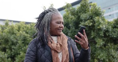 Kıdemli Afrikalı Amerikalı kadın telefonda selamlıyor. Plaza 'da çantasıyla gülüyor ve dinliyor. Kentsel, yaşam tarzı, çağdaş, iletişim, son sınıf, boş zaman, canlı