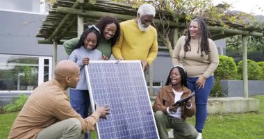 Avluda diz çöken güneş uzmanı ve güneş panelini inceleyen siyah aile faydalarını araştırıyor. Yenilenebilir, sürdürülebilir, teknoloji, yenilik, eğitim, açık hava, toplum