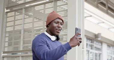 Afro-Amerikalı adam dışarıda akıllı telefonları selamlıyor, ekranı tıkırdatıyor ve ses üstüne ses çıkarıyor. Teknoloji, iletişim, kentsel, gelişigüzel, yenilik, bağlantı, gençlik