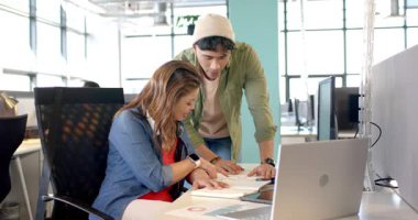 Çalışma masasının yakınındaki çeşitli iş arkadaşları çizelgeleri kontrol ediyor ve düzenleme incelemesi için ekrana işaret ediyor. İşbirliği, takım çalışması, ofis, profesyonel, modern, iletişim, analiz