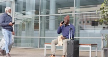 Afro-Amerikalı gezginler, terminalin dışındaki bankta duran bavulların yanında telefonla yol soruyorlar. Gezginler, ulaşım, kentsel, çağdaş, iletişim, yaşam tarzı, bağlantı