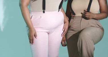 Farklı bayan arkadaşlar, stüdyo kameraları yukarı bakarken pantolon askılarını düzeltip gülüyorlar. Arkadaşlık, işbirliği, moda, portre, gündelik, çeşitlilik, pozitiflik