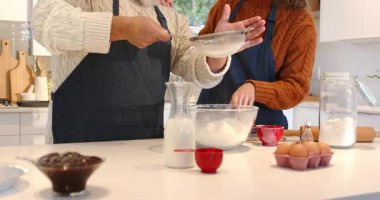 Pişirme hazırlıkları, mutfak adasında kek hamuru hazırlarken elek ile un eleme. Mutfak, yemek pişirme, hazırlık, yerli, rahat, enerjik, takım çalışması.