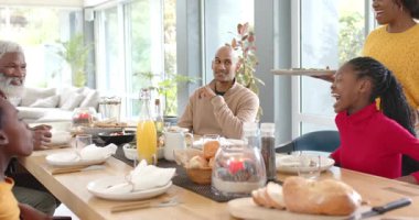 Farklı aileler sakallı adamı karşılarken siyahi bir kadın masada alkış ve yemek servisi duyuyor. Aile toplantısı, aile sahnesi, kutlama, sıcaklık, birliktelik, yaşam tarzı, iç mekan.