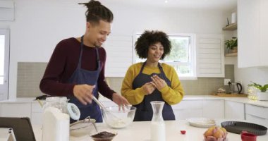 Tezgahta duran önlüklü bir çift tablete bakıyor, süt döküyor ve pişirmek için un karıştırıcı hamurlar ekliyor. İşbirliği, yerli, aşçı, neşeli, yenilikçi, yaşam tarzı, modern