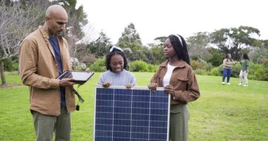Çimenlikteki güneş paneli kablolarını kontrol eden kızlarına rehberlik eden farklı bir aile. Aile, eğitim, yenilenebilir enerji, sürdürülebilirlik, açık hava, teknoloji, yenilik