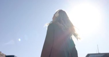 Şehir caddesinde, temiz gökyüzünün altında yürüyen bir kadın, güneşin parladığını, yavaşladığını, kulaklıkları ayarladığını fark ediyor. Açık hava, boş zaman, moda, gündelik, canlı, yaşam tarzı, teknoloji