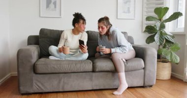 Çeşitli bayan arkadaşlar akıllı telefon görüntülerini paylaşıyorlar. Güneşli gri kanepede fincanlardan gülüp yudumluyorlar. Samimi, rahat, enerjik, dostluk, rahatlama, rahat, yaşam tarzı