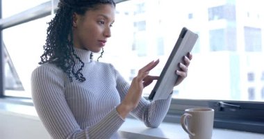 Afro-Amerikalı kadın tableti kaldırıyor ve bardakta kayıyor içeriği keşfediyor, gülümsüyor. Teknoloji, yaşam tarzı, minimalist, şehir, rahatlama, iletişim, bağlılık