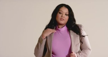 Kamera kayıtta, 30 'lu yaşlardaki kadın bej ceketini ayarlıyor, saçlarını süpürüyor, stüdyoda gülümsüyor. Profesyonel, kendine güvenen, zarif, minimalist, iş, portre, çeşitlilik