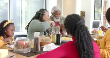 Çeşitli aile yemeği başlatıyor, yemek masasında ahşap maşayla ortak kaseden makarna uzatıyor. Aile, mutfak, birliktelik, sıcaklık, çok kültürlü, sade, beslenme.