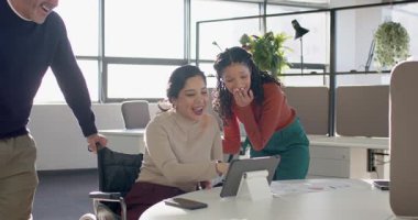 Çeşitli iş arkadaşları tekerlekli sandalyede tablet ekrana bastırıyor, inceleme için ofiste toplanıyorlar. İşbirliği, erişilebilirlik, yenilik, takım çalışması, modern, kapsayıcı, teknoloji