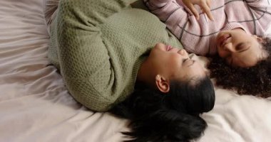 Anne ve kızı yatakta sohbet ederken kız akıllı telefon kaldırıyor, anne de şakaya gülüyor. Aile, samimiyet, bağlantı, rahatlama, sıcaklık, samimiyet, sohbet