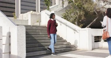 Şehir meydanında beton merdivenlerden inen bir adam, kadın bavulunu sarılmak için yuvarlarken duruyor. Kentsel, dostluk, bağlantı, modern, gündelik, açık hava, canlı