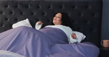 Uyandıktan sonra bir kadın battaniyeyi yatağa itti, kollarını uzattı, uyanmak için yüzünü ovuşturdu. Rahatlık, rahatlık, huzur, konfor, rahatlık, rahatlık, rahatlık, çağdaş