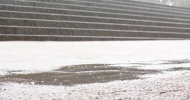 Asfalt üzerinde yürüyen yağmurun oluşturduğu su birikintisine adım atan Afrikalı Amerikalı bir adam. Kentsel, ıslak, ayakkabılı, karamsar, dokulu, hareketli, çevresel