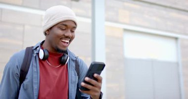 20 'li yaşlarda Afro-Amerikan bir adam akıllı telefon kaldırıyor, gülümsüyor ve binaya doğru kayıyor. Teknoloji, yaşam tarzı, modern, gündelik, kentsel, dijital, boş zaman