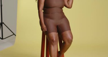 Kamera önünde Afrika kökenli Amerikalı kadın sarı arka planda cilt bakımı için omuz masajı yapıyor. Portre, sağlık, fitness, yaşam tarzı, doğal, sağlık, güzellik