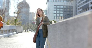 Bariyere yaslanmış yürüyen bir kadın akıllı telefonu arıyor kahve fincanının yanındaki çantayı düzeltiyor. Kentsel, yaşam tarzı, samimi, modern, gündelik, iletişim, mimari