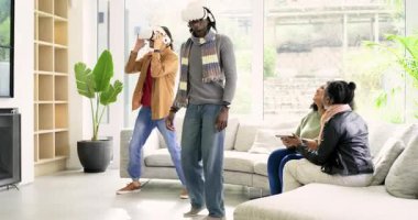 Çeşitli erkekler VR kulaklıklarını takıyor ve oturma odasında VR oyunu oynarken çeşitli kadınlar gülüyor. Fütürist, sürükleyici, sosyal, eğlence, modern, etkileşim, eğlence