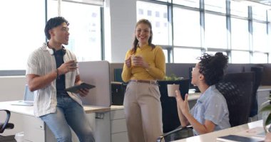 Çeşitli iş arkadaşları açık planlı ofiste kahve içip bardakları kaldırıyor ve tabletleri tıkırdatıyor. İşbirliği, takım çalışması, yoldaşlık, verimlilik, iletişim, modern, canlı