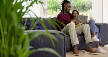 Afro-Amerikalı erkek ve Hintli kadının evdeki kanepede tablete dokunuşlarını bulanıklaştıran bitki gibi. Rahat, rahat, modern, teknoloji, bağlantı, rahatlama, yaşam tarzı
