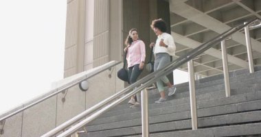 Kız arkadaşlar binanın merdivenlerinden iniyor, akıllı olanları kontrol ediyor ve spor çantalarıyla dışarı çıkıyorlar. Fitness, activewear, urban, modern, takım çalışması, motivasyon, refah