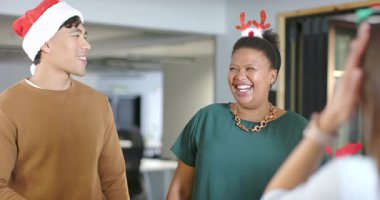 Noel Baba şapkalı ve boynuzlu çeşitli iş arkadaşları masa başında sohbet ediyor, çerçeveye girerken gülüyorlar. Kutlama, dostluk, şenlik, tatil, takım çalışması, neşeli, sıradan