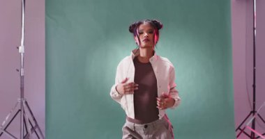 Stüdyoda yeşil arka planda poz veren şık kıyafetli kendine güvenen bir kadın. Moda, tarz, güven, modellik, portre, fotoğraf çekimi