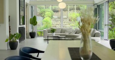 Kamera, tahta masanın üzerinde kurumuş çimenlerin olduğu cam vazoyu öne doğru itiyor ve odaklanıyor. Minimalist, iç tasarım, doğal dekor, modern ev, botanik, mimari, sükunet