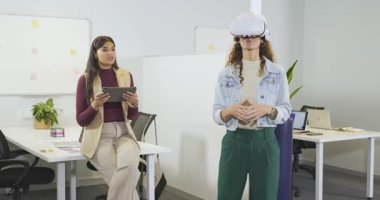 Çeşitli kadın iş arkadaşları VR tanıtımını kolaylaştırmak için tablet kullanıyor ve kullanıcı jestlerine rehberlik ediyor. Teknoloji, işbirliği, yenilik, modern, profesyonel, etkileşim, geleceksel