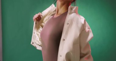 Şık ceketli genç bir kadın stüdyoda yeşil arka plana karşı güvenle poz veriyor. Moda, tarz, portre, güven, giysi, moda