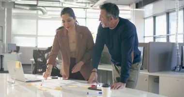 Çeşitli iş arkadaşları işaretleri göstererek notları yeniden düzenliyor ve ofiste planlama için laptopa danışıyorlar. İşbirliği, beyin fırtınası, takım çalışması, strateji, üretkenlik, yenilik, yaratıcı süreç