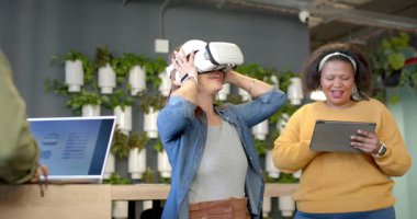 Meslektaşı tableti takip ederken beyaz VR kulaklık takan ve el sallayan orta yaşlı bir kadın. Teknoloji, yenilik, işbirliği, dalma, fütürizm, dijital, yaratıcılık