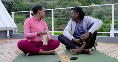 Afro-Amerikalı arkadaşlar şişe kapağını büküyorlar, şişe suyu içiyorlar ve çatı katında sohbet ediyorlar. Sağlık, açık hava, spor, rahatlama, yoldaşlık, doğa.