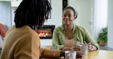 Afro-Amerikalı çift, oturma odasındaki masada el ele tutuşurken kahve fincanlarını kaldırıp sohbet ediyorlar. Romantik, samimi, samimi, samimi, bağlantı, sevgi, samimi