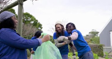 Çeşitli gönüllüler gülerken otları ayıklıyor ve çarşafın altındaki yatağı temizlemek için torba dolduruyorlar. Topluluk, takım çalışması, sürdürülebilirlik, doğa, açık hava, işbirliği, çevre